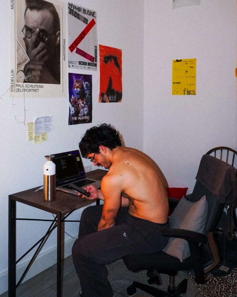 Bingen at his desk, side profile, posters on the wall behind him.